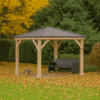 Wooden gazebo with a dark metal pitched roof and decorative braces, sheltering a black bench, set on a lawn covered with yellow fallen leaves, surrounded by evergreen hedges and trees with vibrant autumn foliage.