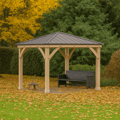 Wooden gazebo with a dark metal pitched roof and decorative braces, sheltering a black bench, set on a lawn covered with yellow fallen leaves, surrounded by evergreen hedges and trees with vibrant autumn foliage.