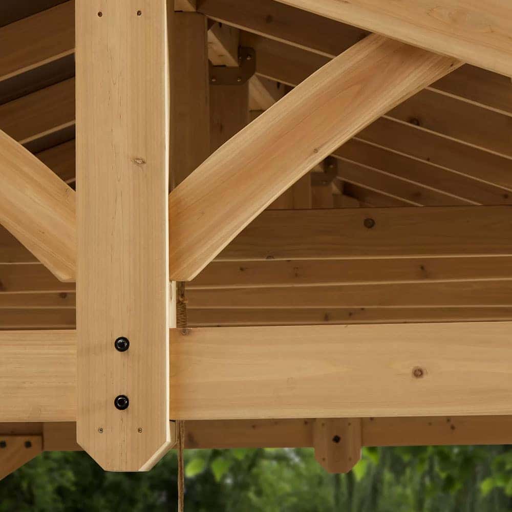 Close-up of interlocking wooden beams joined with metal bolts, featuring curved and angled elements, set against a green outdoor backdrop.