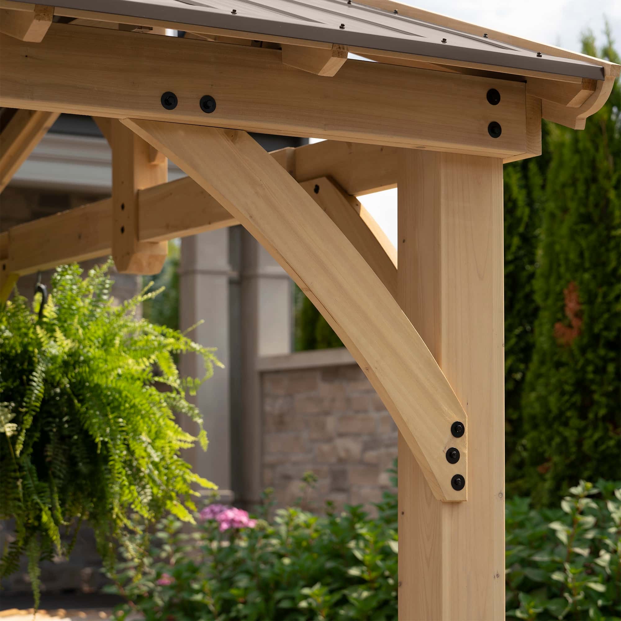 Close-up of wooden pergola corner joint with light timber, black bolts, and diagonal support brace.