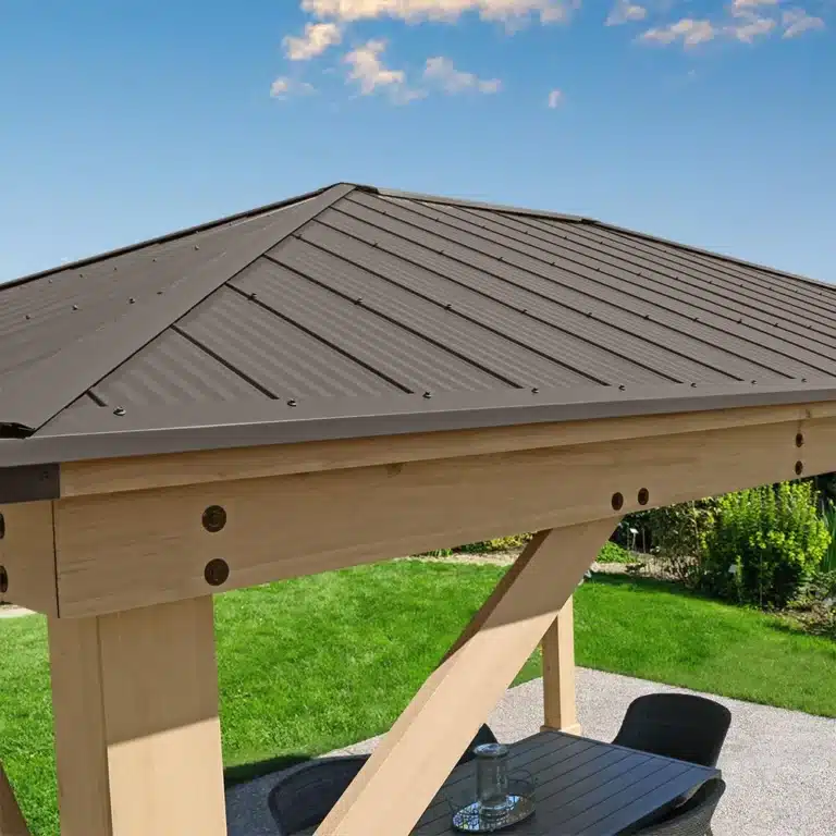 Close-up of a wooden gazebo roof with dark metal panels and bolt-secured beams, overlooking a patio with outdoor furniture and garden lawn.