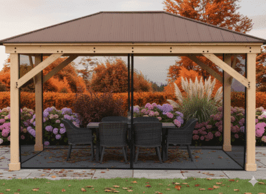 Wooden gazebo with a metal roof and string lights, featuring a dining table with six black wicker chairs on a dark outdoor rug, surrounded by purple hydrangeas, ornamental grasses, and autumn trees with red and orange foliage.