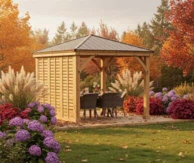 Wooden gazebo with dark aluminium roof, single wooden wall, and outdoor seating nestled in a lush UK garden with vibrant autumn foliage.