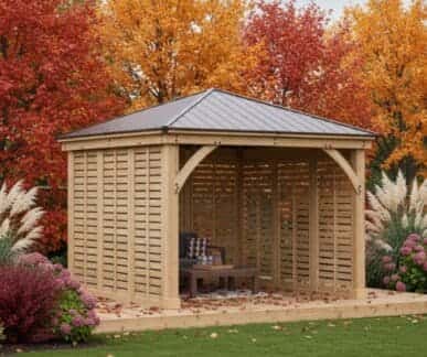 Wooden gazebo with vertical slats and a dark metal hip roof, featuring a bench with a chessboard, surrounded by autumn foliage and flowering plants in a landscaped garden.