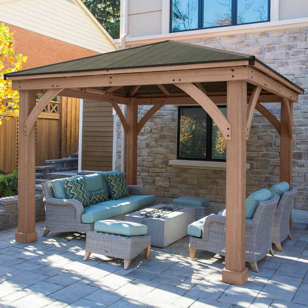Wooden gazebo with dark roof and light blue cushioned wicker furniture on stone patio