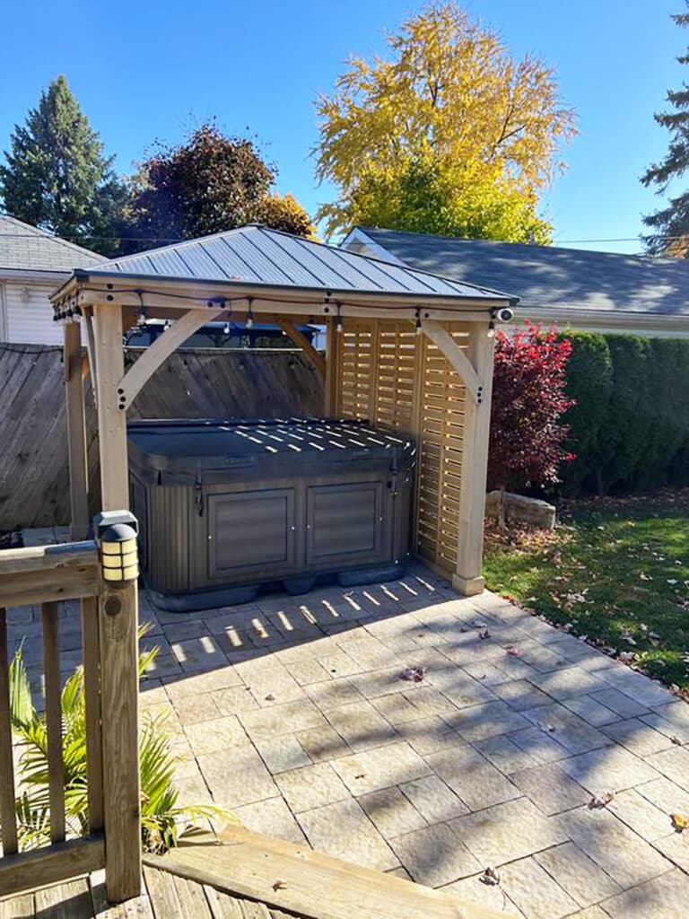 Covered hot tub beneath timber pergola with slanted roof and autumn garden backdrop