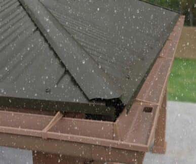 Corrugated metal roof with visible rain droplets and a brown gutter system attached, suitable for costco gazebos set against a blurred outdoor background with trees and fencing.