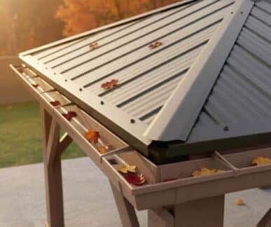 Close-up of a corrugated metal gazebo roof with scattered autumn leaves and a gutter system, set against a grassy area and trees with fall foliage.