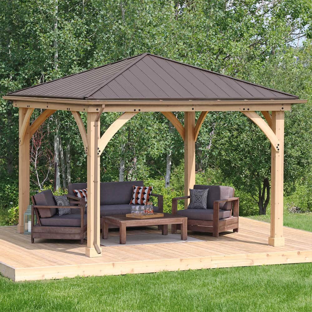 Timber gazebo with dark metal roof and curved braces on wooden deck, featuring cushioned seating and coffee table in garden setting