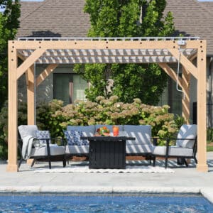 Wooden pergola with slatted roof over cushioned armchairs and fire pit table, set beside a swimming pool with lush garden and hydrangeas in the background.