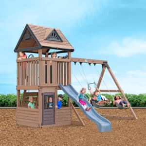 Wooden children’s playset with slide, swings, and multi-level structure in a garden setting with children playing.