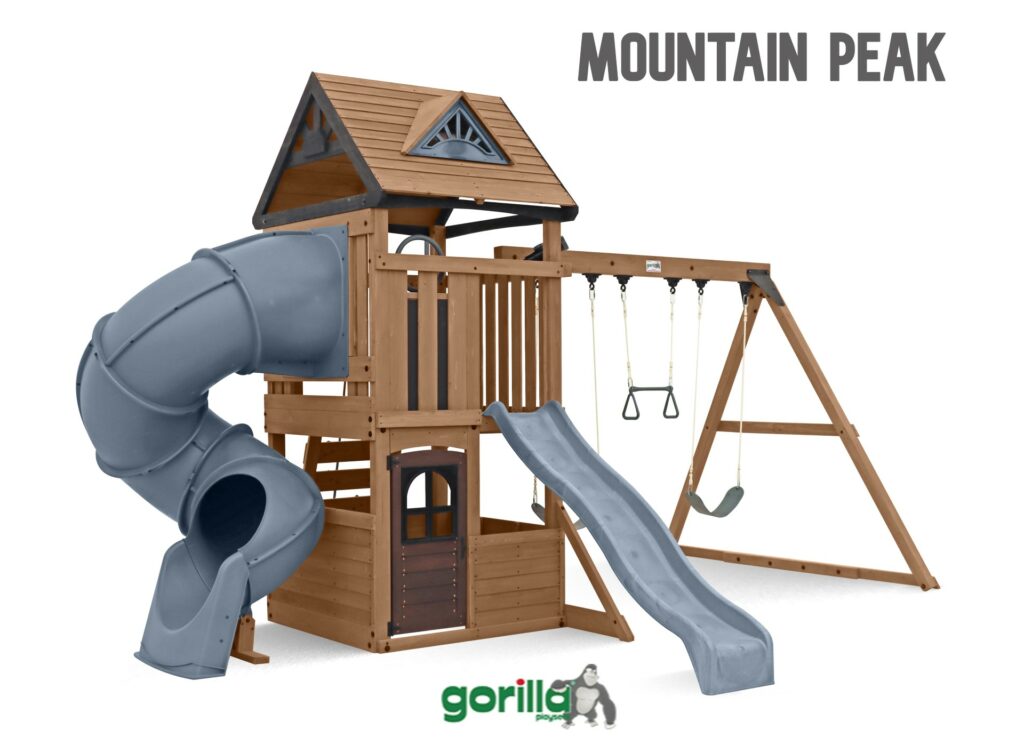This is a product image featuring a large, wooden swing set and play structure named "MOUNTAIN PEAK". This structure combines features from the two previous designs.

Key Features:
Play Structure (Fort): The central fort is a two-level wooden structure, built from stained wood.

The upper level is a tower with railings, capped by a decorative roof with dark brown shingles and a triangular vent/window.

The lower level is an enclosed playhouse area with a small, dark wooden plank door.

Slides: This structure uniquely features two slides extending from the upper level:

A grey/blue, enclosed tube slide spirals down from the left side.

A straight, grey/blue plastic slide extends from the front.

Swing Beam: An angled A-frame swing beam is attached to the main fort structure on the right side.

It supports two standard belt swings and a trapeze bar with hand grips.

Materials and Style: The entire structure has a consistent, natural, stained wood finish.

Branding: The name "MOUNTAIN PEAK" is displayed in large, dark grey text at the top right, and the "gorilla play sets" logo is in the bottom centre.