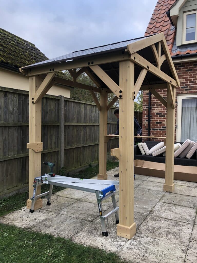 Wooden grill gazebo being installed on a garden patio with tools and ladder in view