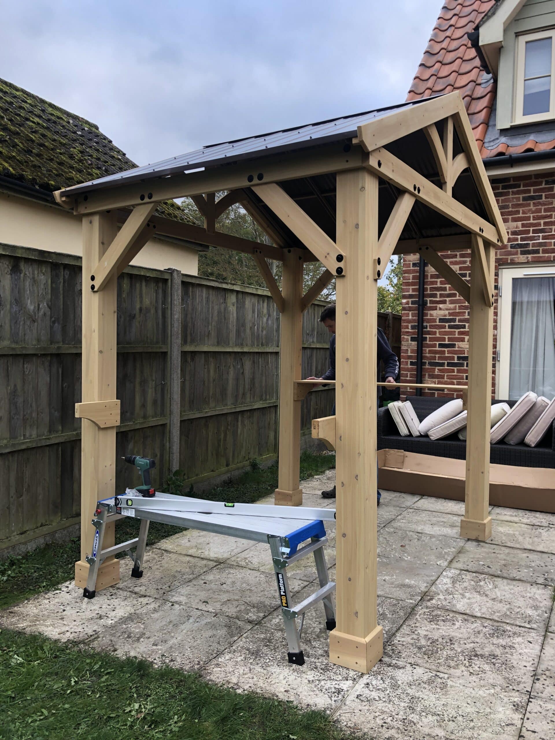 Wooden grill gazebo being installed on a garden patio with tools and ladder in view