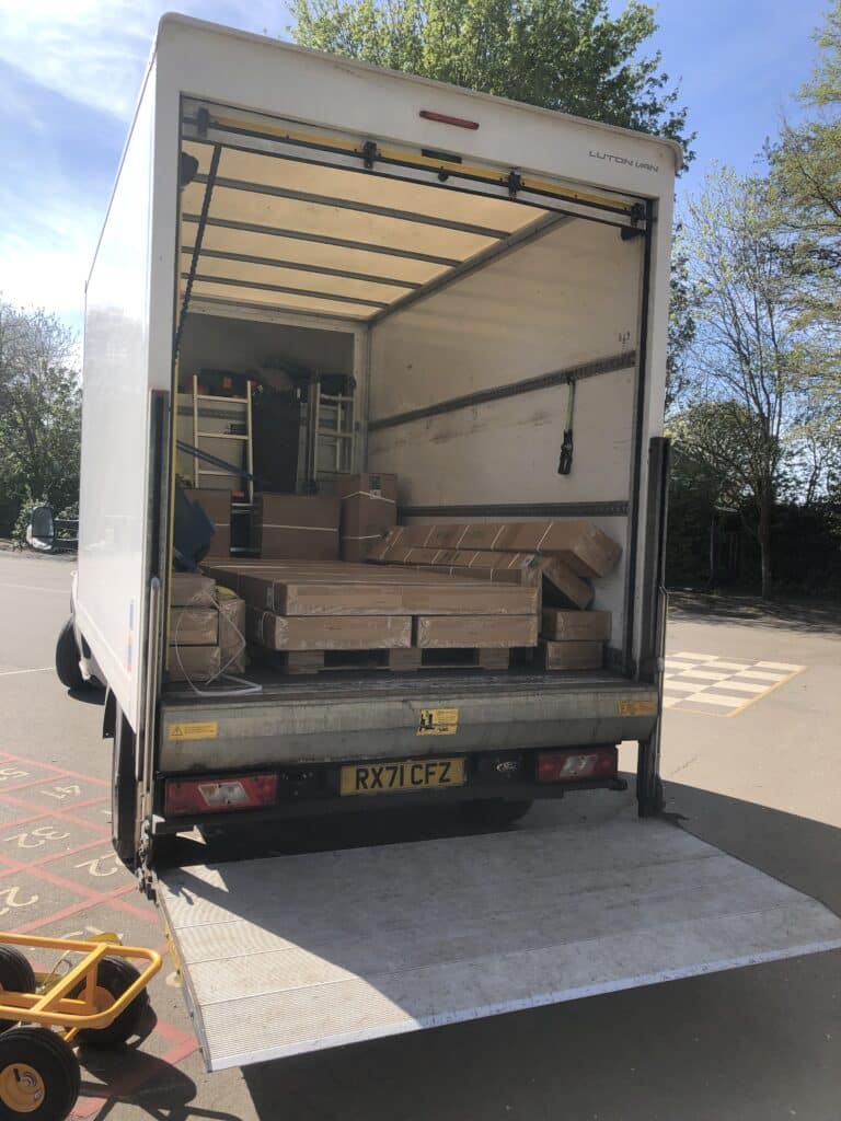 Open white box truck with cardboard boxes inside and a metal ramp extended, parked in a paved area during a sunny day.