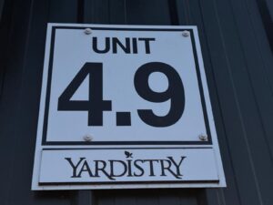 Sign reading “Unit 4.9 Yardistry” mounted on a dark vertical-paneled wall.
