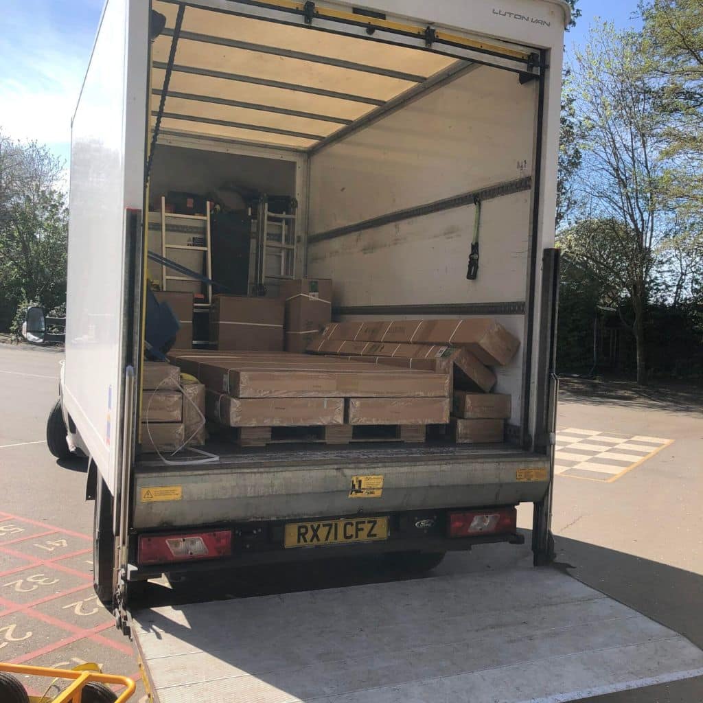 Open white box truck with cardboard boxes inside and a metal ramp extended, parked in a paved area during a sunny day.
